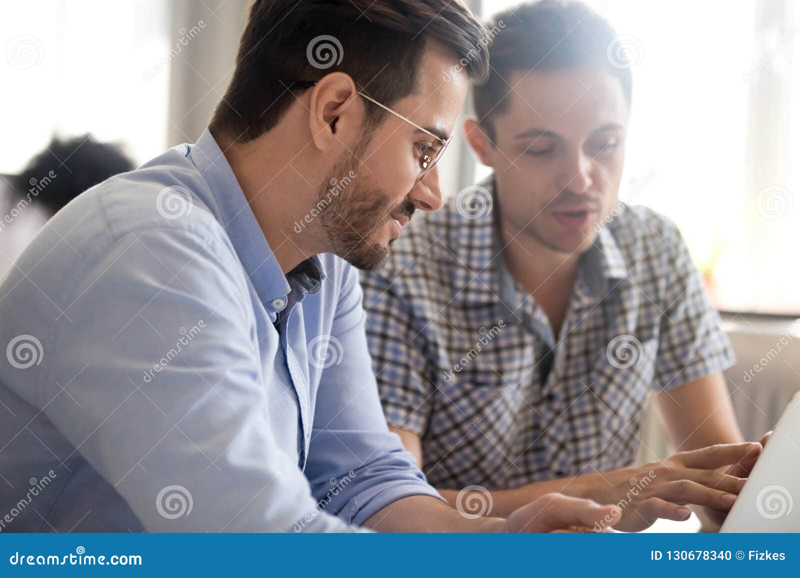 focused male colleagues work together using laptop discussing on