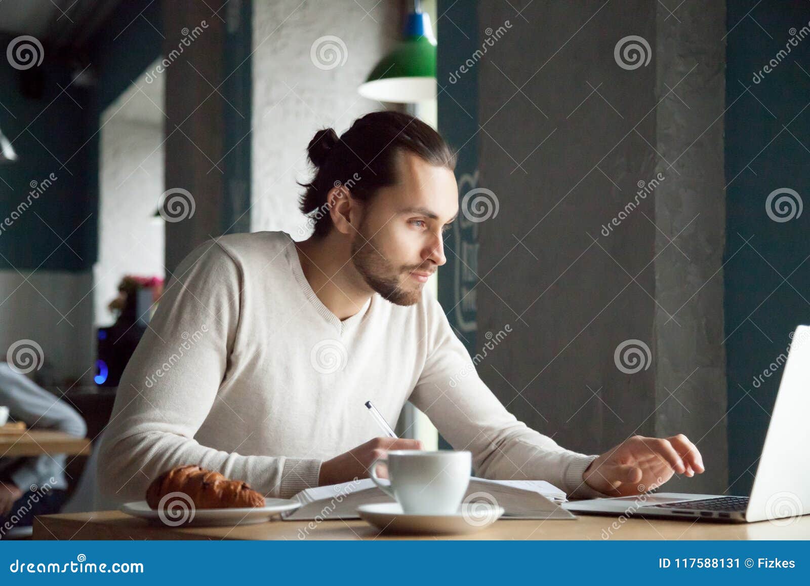 focused man writing notes learning online with laptop in cafe