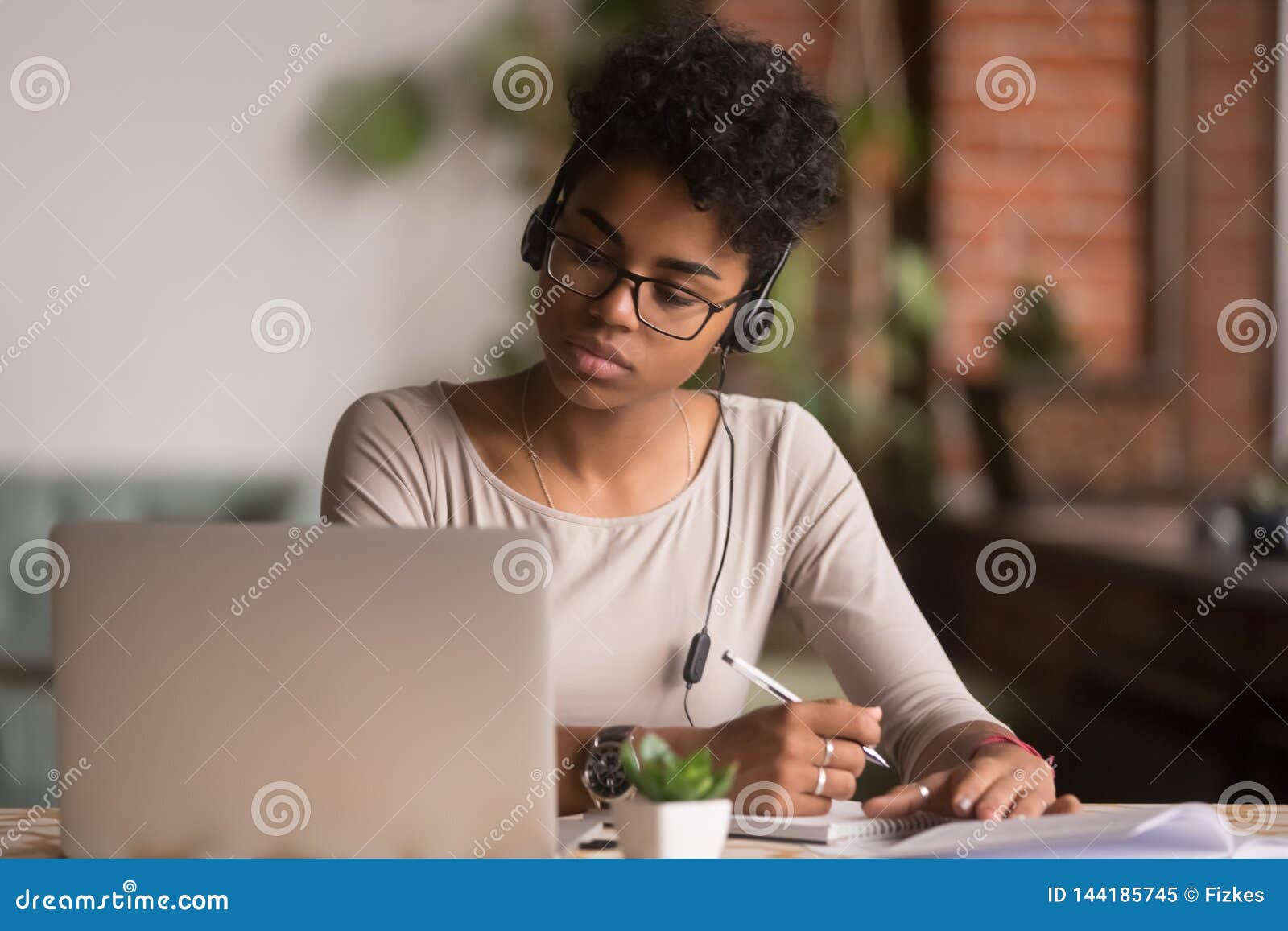 focused mixed race woman wearing headphones watching webinar write notes