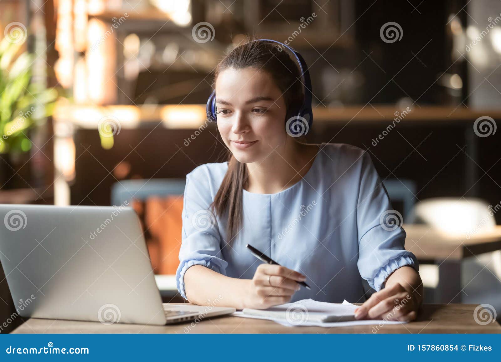 focused woman wearing headphones using laptop, writing notes