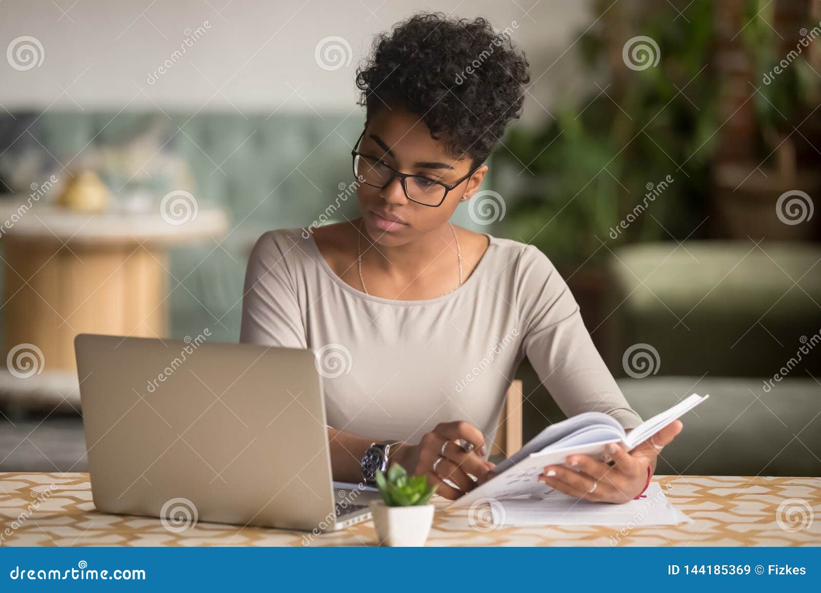 focused african student looking at laptop holding book doing research