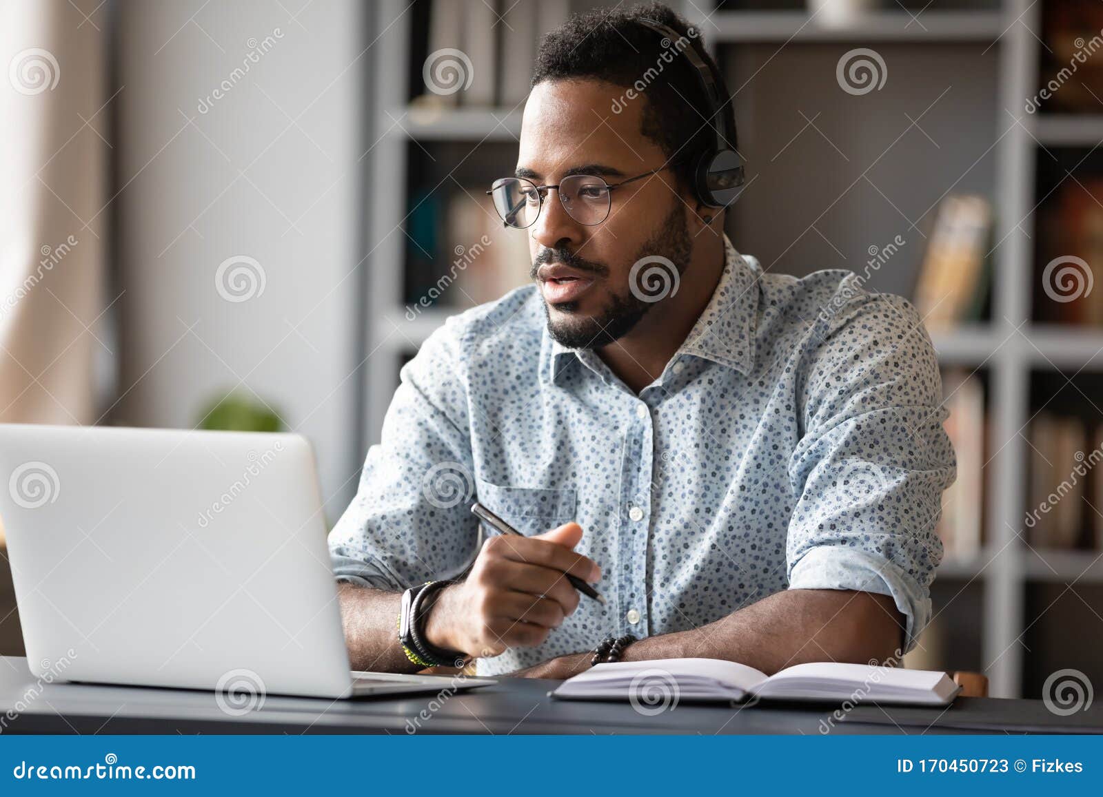 focused african businessman wear headphones study online watching webinar