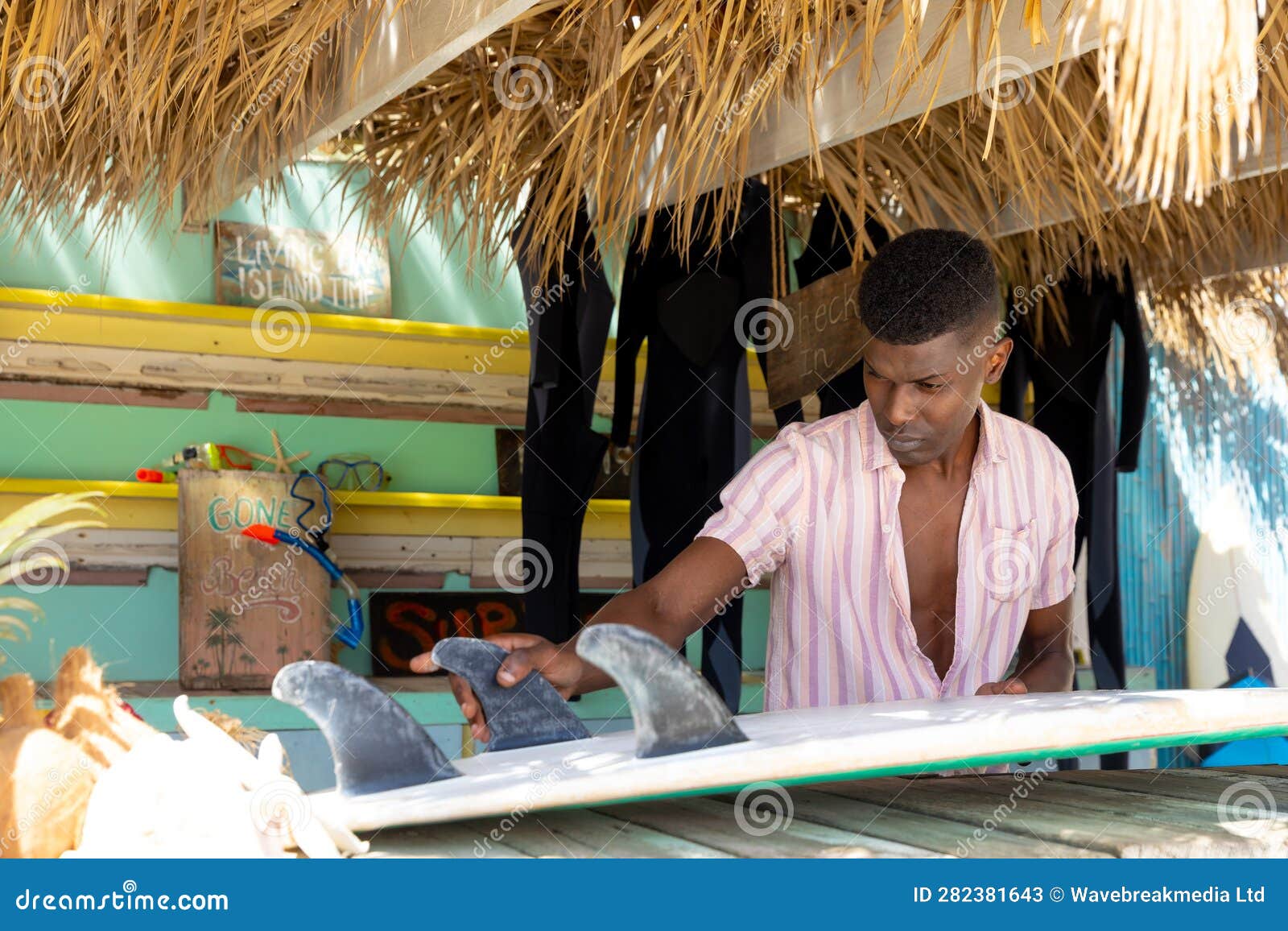 focussed african american man preparing surfboard behind counter of surf hire beach shack