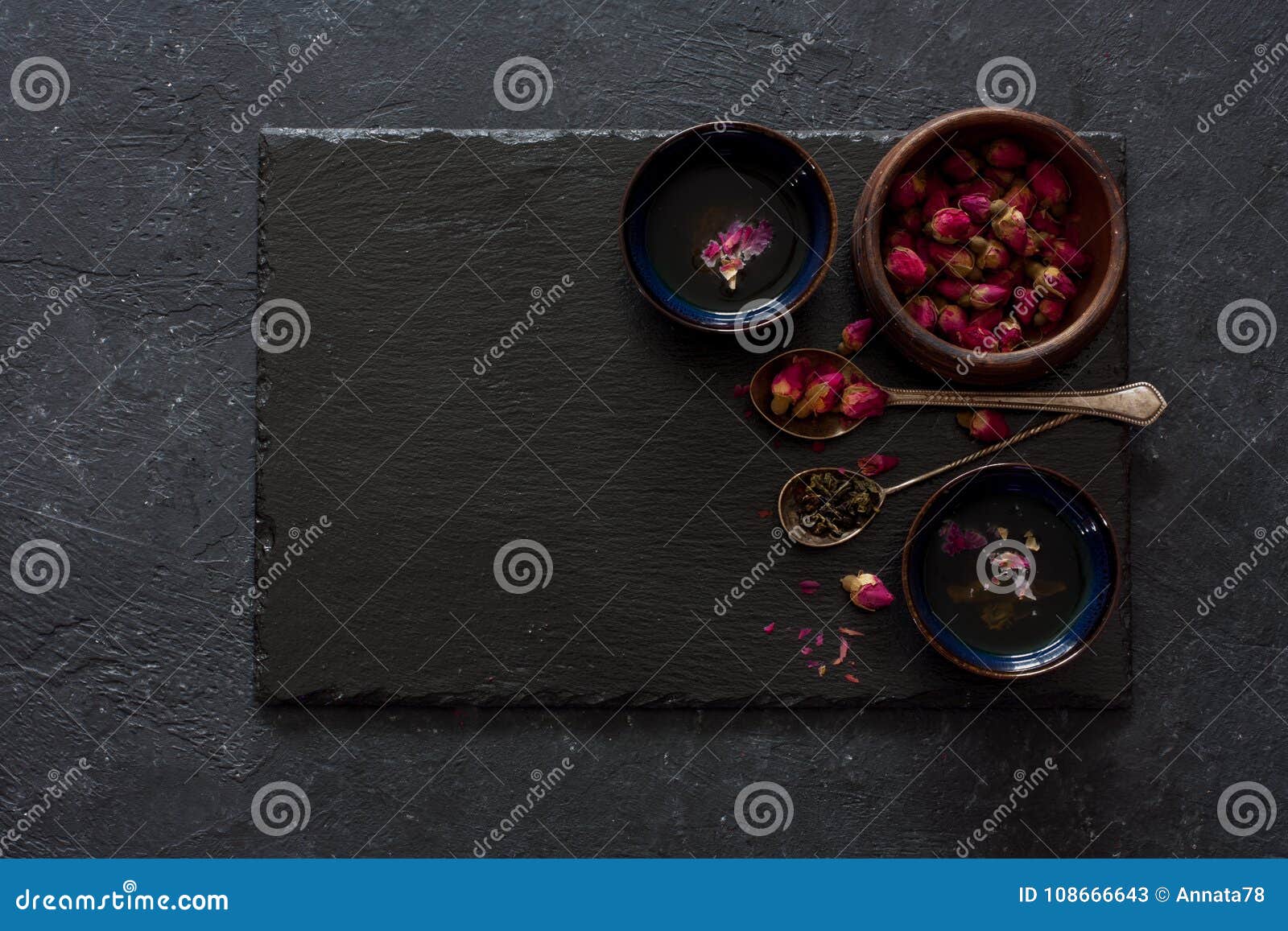 El fondo de piedra negro con las tazas de infusión de hierbas, seca las flores y las cucharas color de rosa del vintage Visión superior Copie el espacio