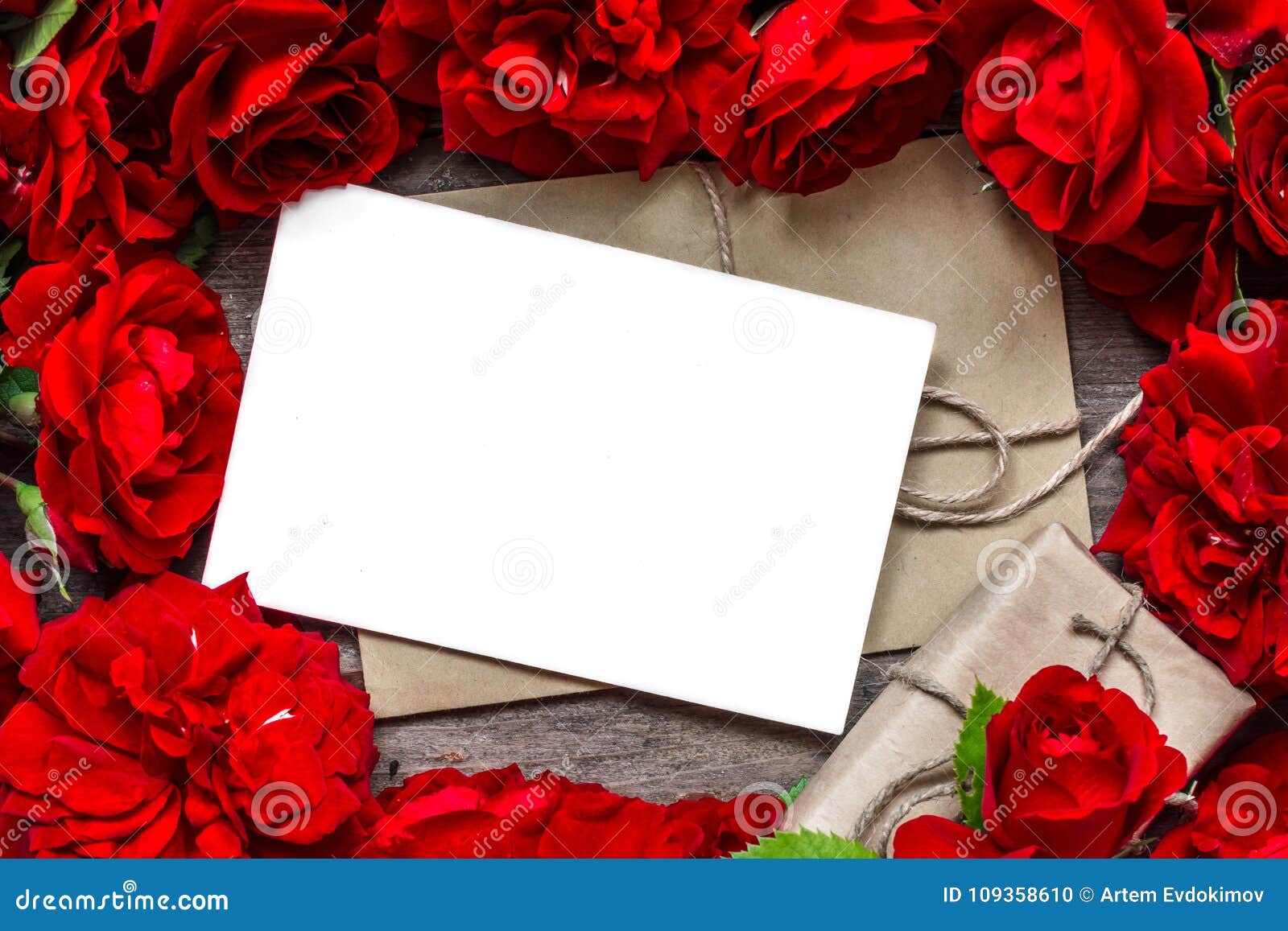 Fondo di giorno di biglietti di S cartolina d'auguri in bianco nel telaio fatto dei fiori delle rose rosse e del contenitore di regalo Derisione su Disposizione piana Vista superiore