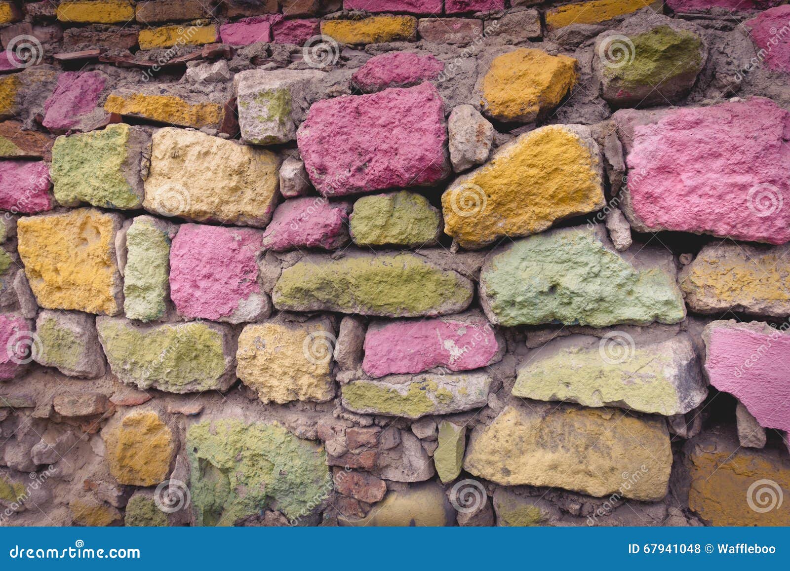 Fondo variopinto di struttura della parete di pietra Vecchio metta il bastone tra le ruote fatto dei blocchi di pietra dipinti luminosi approssimativi