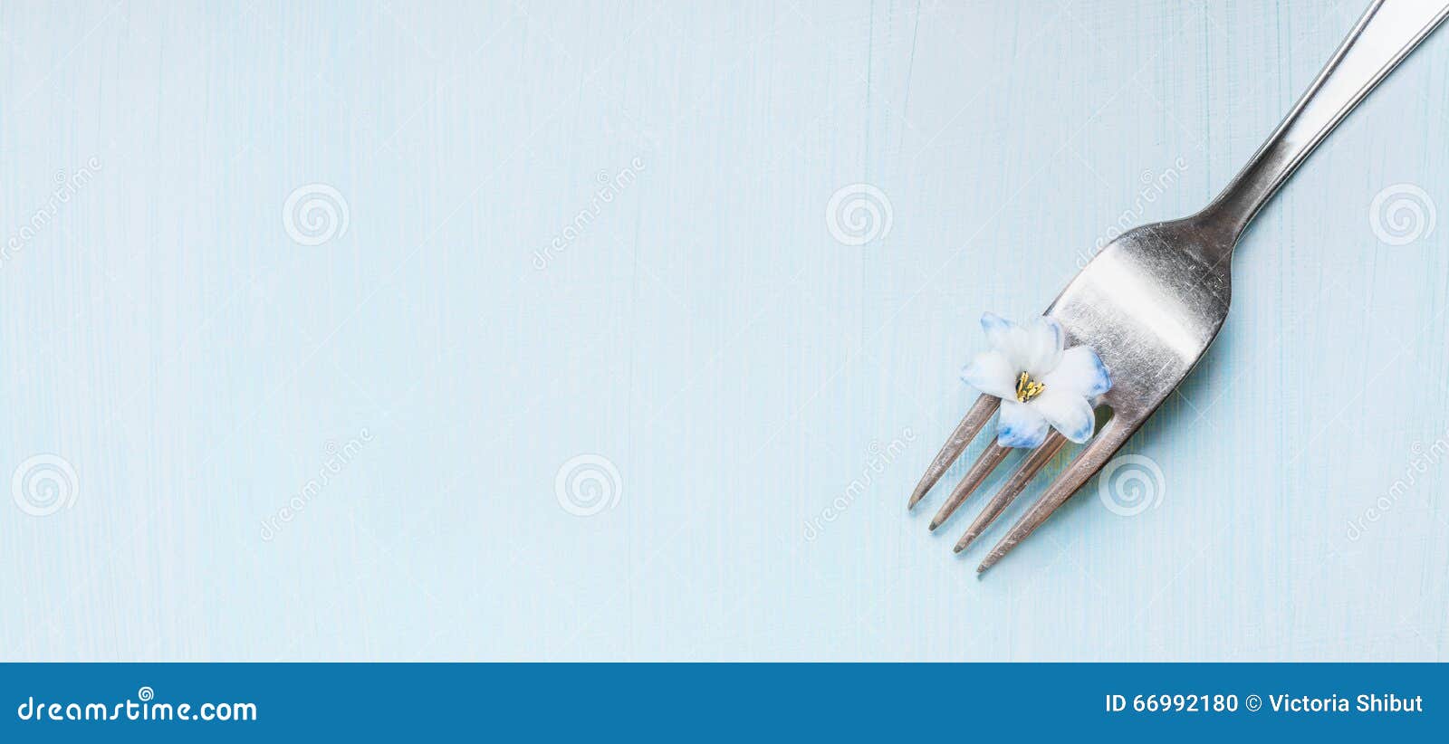 Fork with little blue flower on light green shabby rustic background, top view, banner.