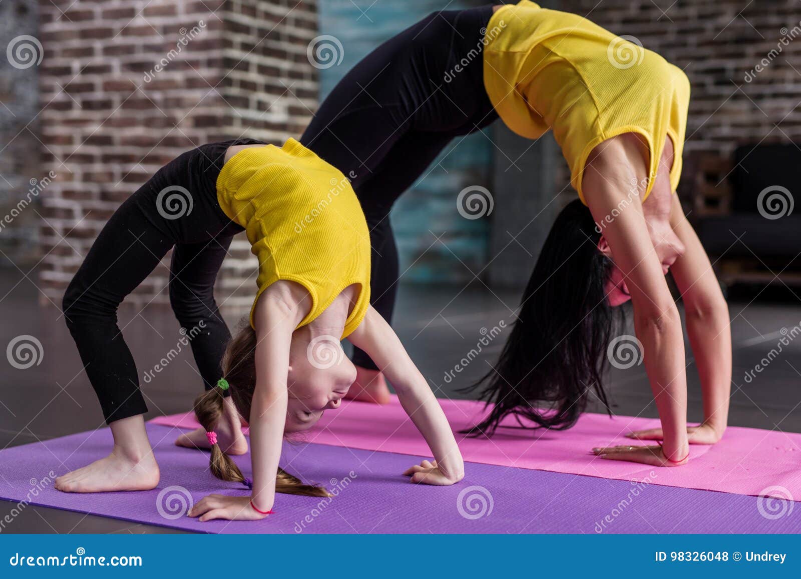 Formazione degli insegnanti femminile di yoga dei bambini una ragazza del bambino che sta nella posa della ruota che risolve nello studio alla moda di sport