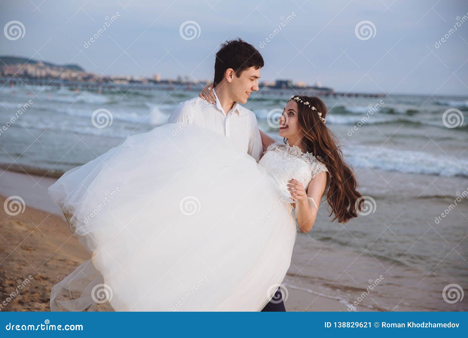 Fornal niesie panny młodej w jego rękach na ocean plaży Właśnie zamężna szczęśliwa para zabawę przy dzień ślubu Pojęcie miłość, miesiąc miodowy