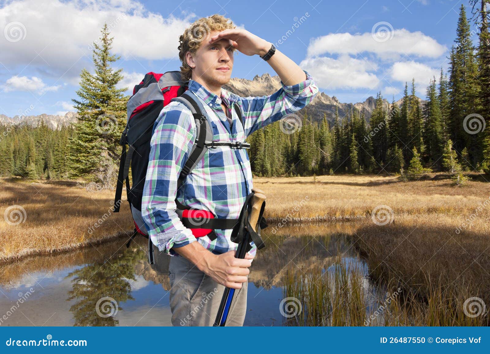 Forscher. Junger Mann mit Spazierstöcken und einem Rucksack bewundert die schöne Landschaft in der Abendleuchte