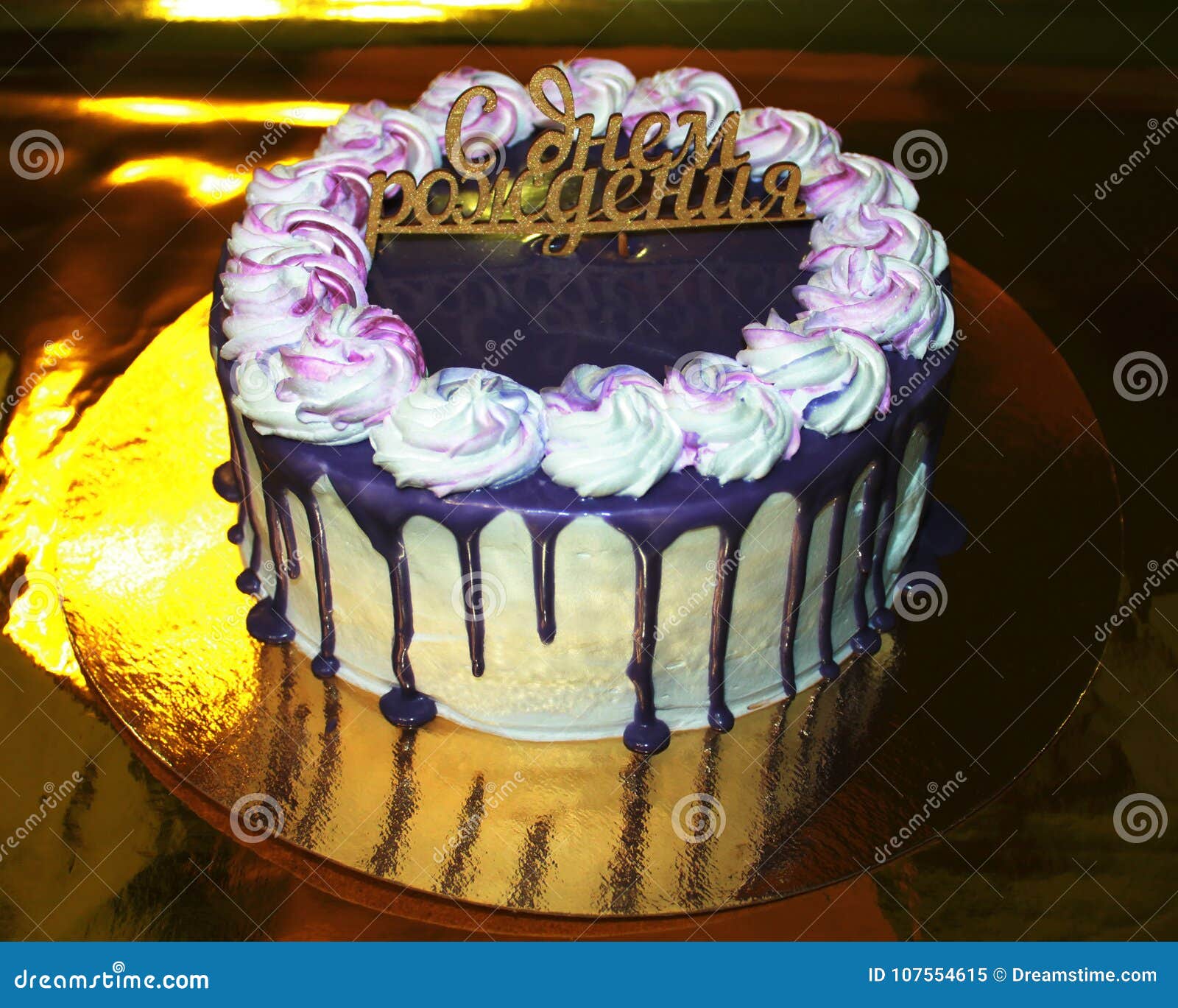 Foto av kakan på en guld- substrate med en guld- bakgrund, lycklig födelsedag. Festlig födelsedagkaka med strimmor av choklad, en violett färg, med den lyckliga födelsedagen för inskrift