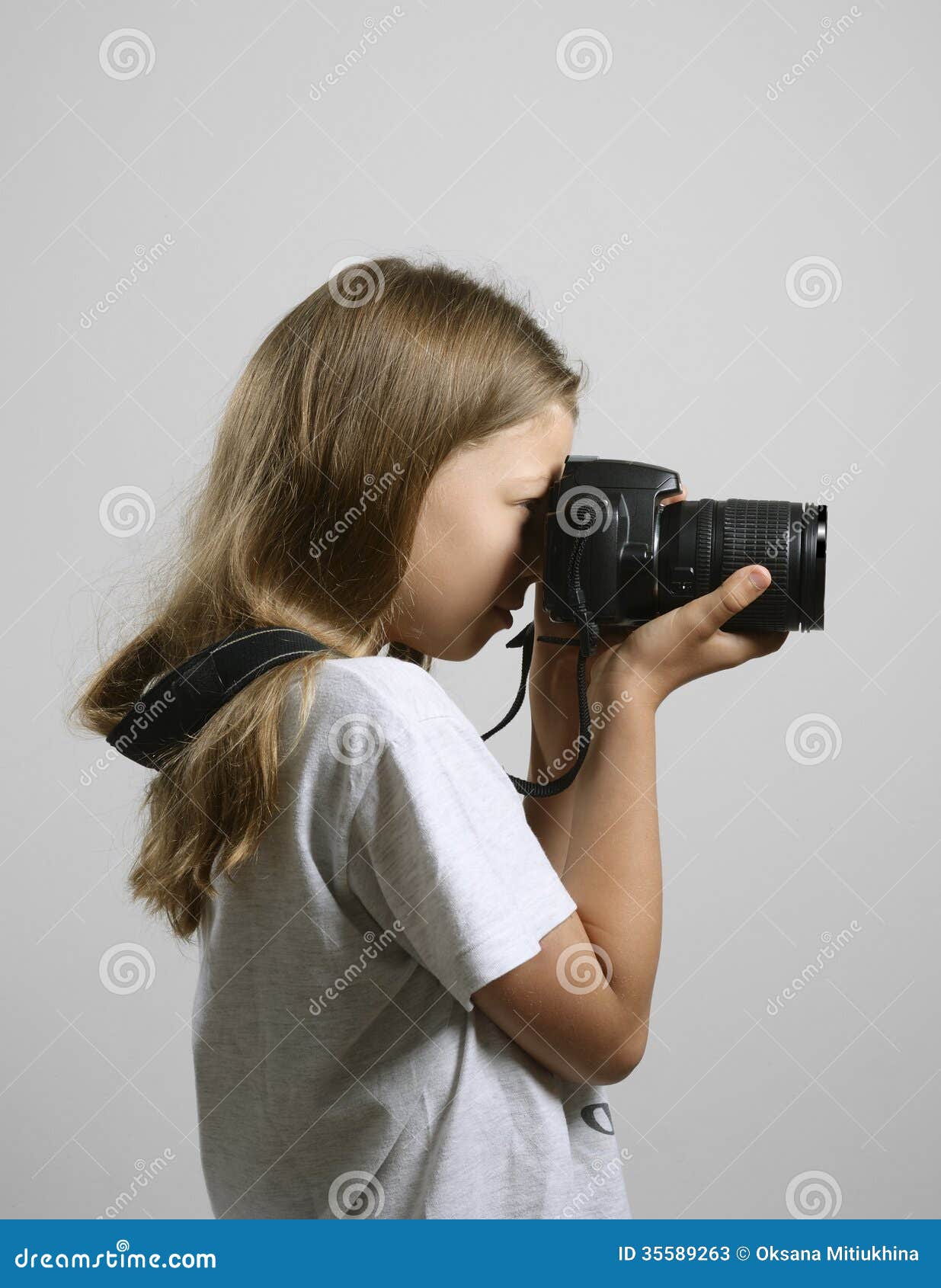 Fotografia da menina do Preteen. Uma menina loura está fotografando com a câmera de SLR no fundo cinzento.