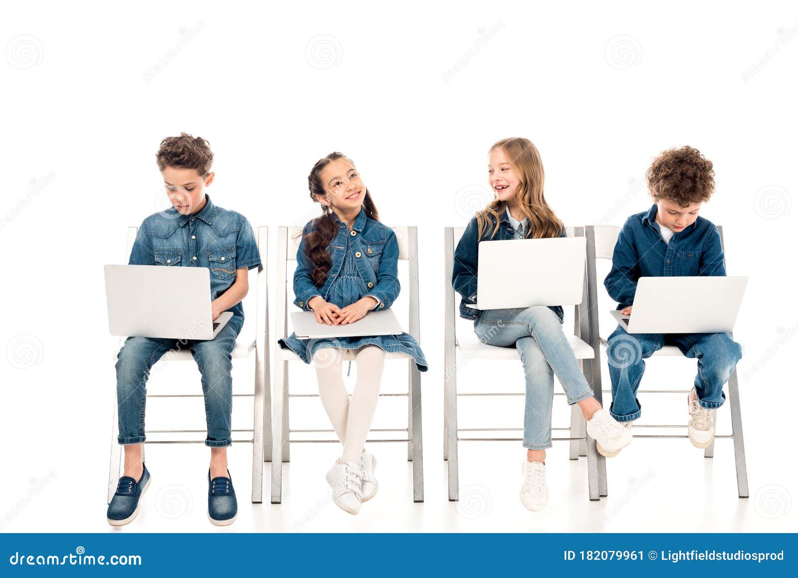 four kids in denim clothes sitting on chairs and using laptops on white.