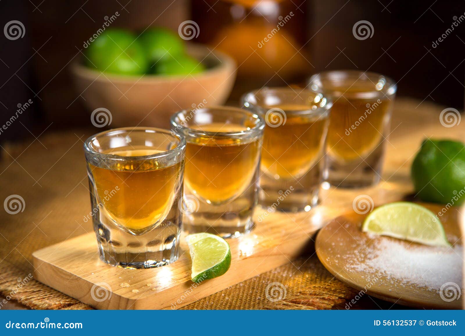 four shot glasses with tequila bottle and bowl of limes with salt at a bar