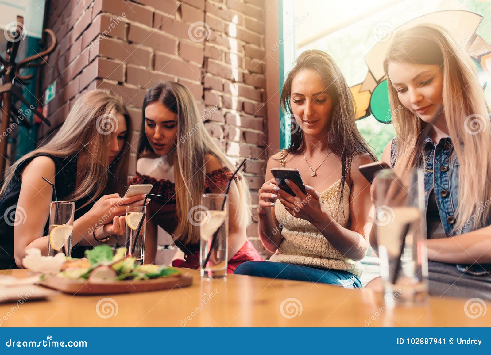 Four Smiling Female Students Sitting in Cafeteria Chatting Using Mobile ...