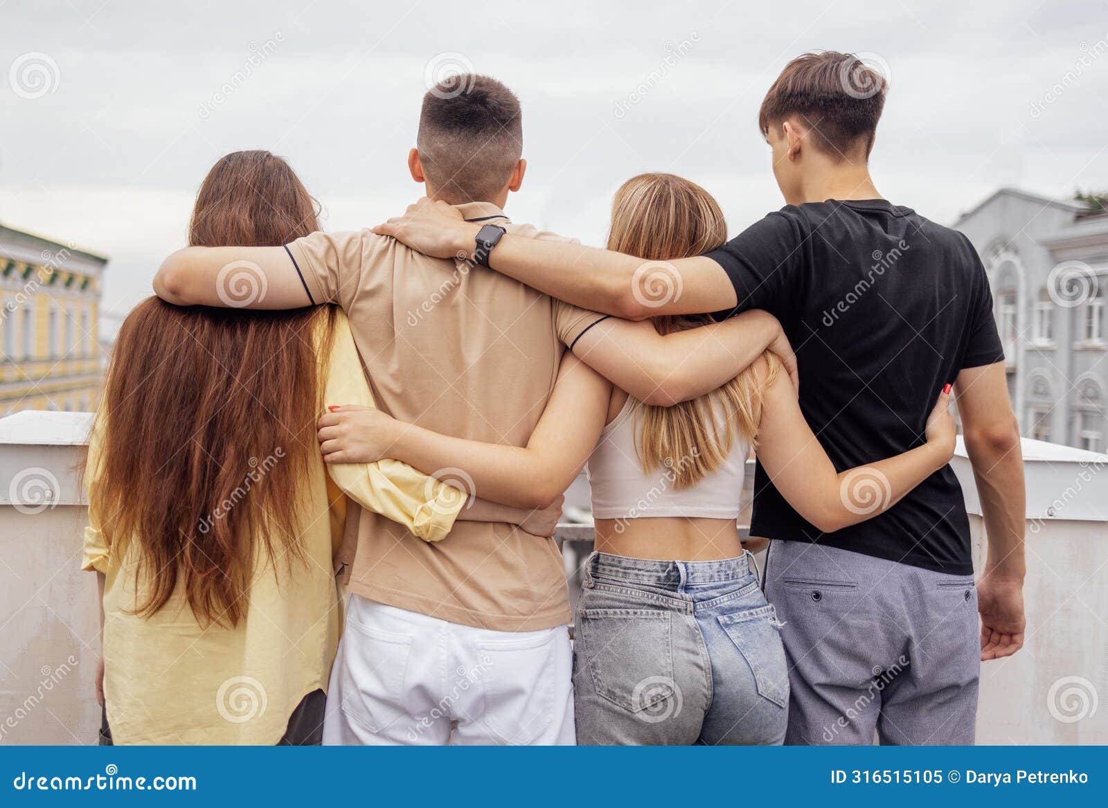 four teenagers hug and stand with their backs on the roof of the house. friends have a great time together