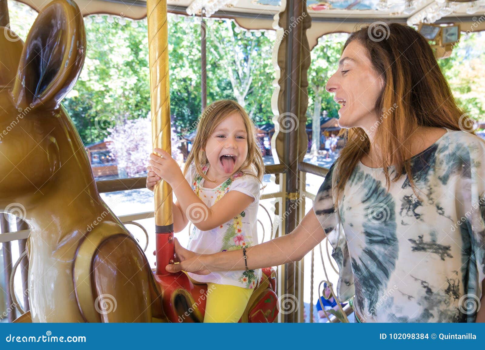 little girl in carousel with mother sticking her tongue out