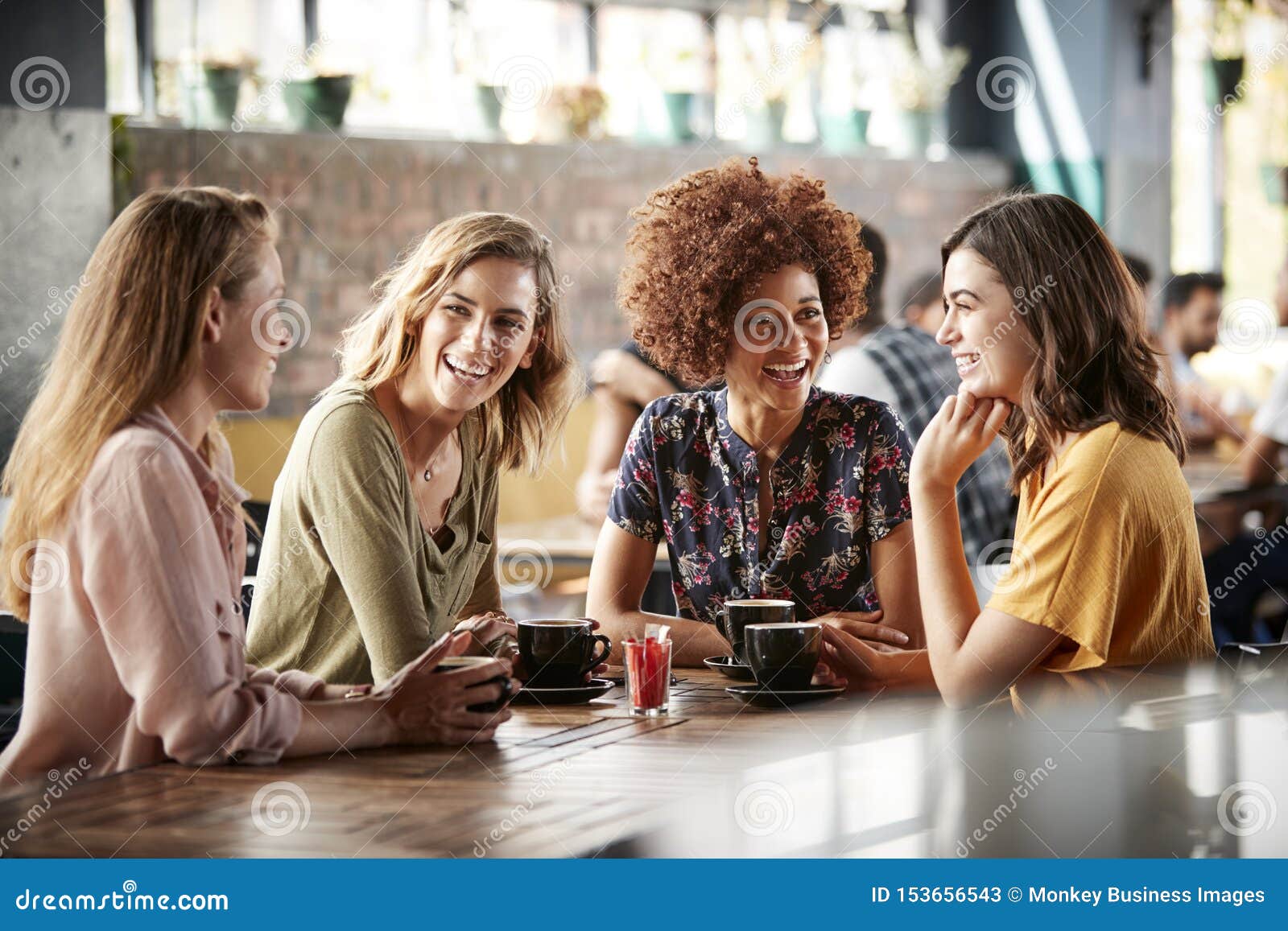 four young female friends meeting sit at table in coffee shop and talk