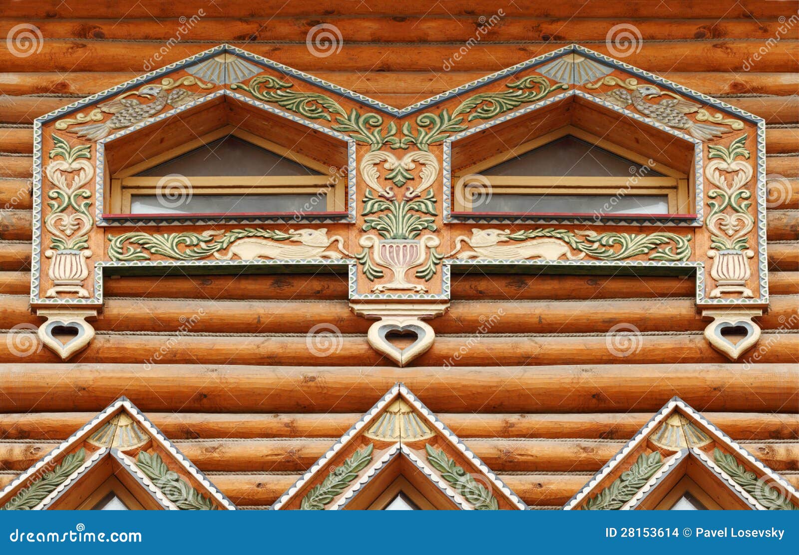 Fragment of large wooden house with carved decoration and two windows.