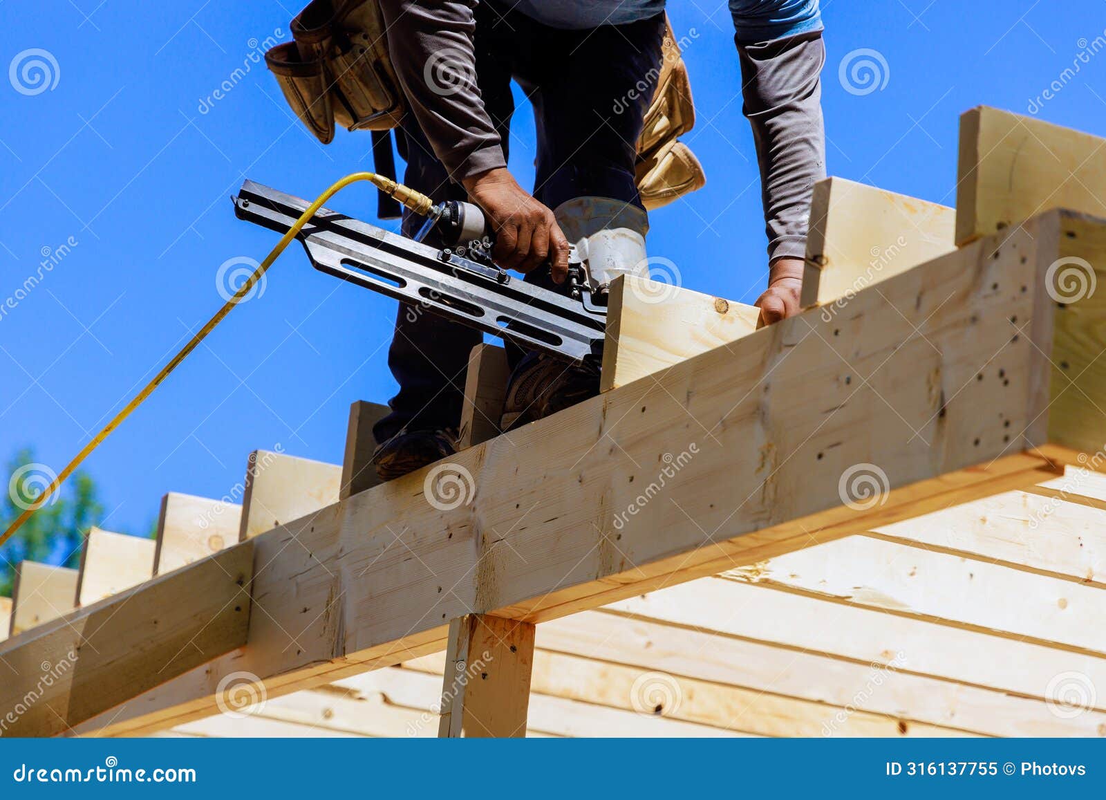 framer worker installing beams using air nails hammer in a nailing wooden frame