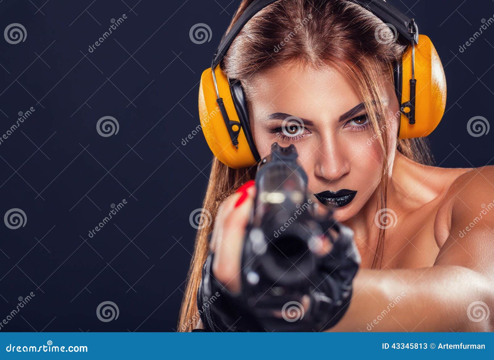 Francotirador. Chica joven hermosa con el entrenamiento negro del maquillaje con una pistola en un fondo oscuro
