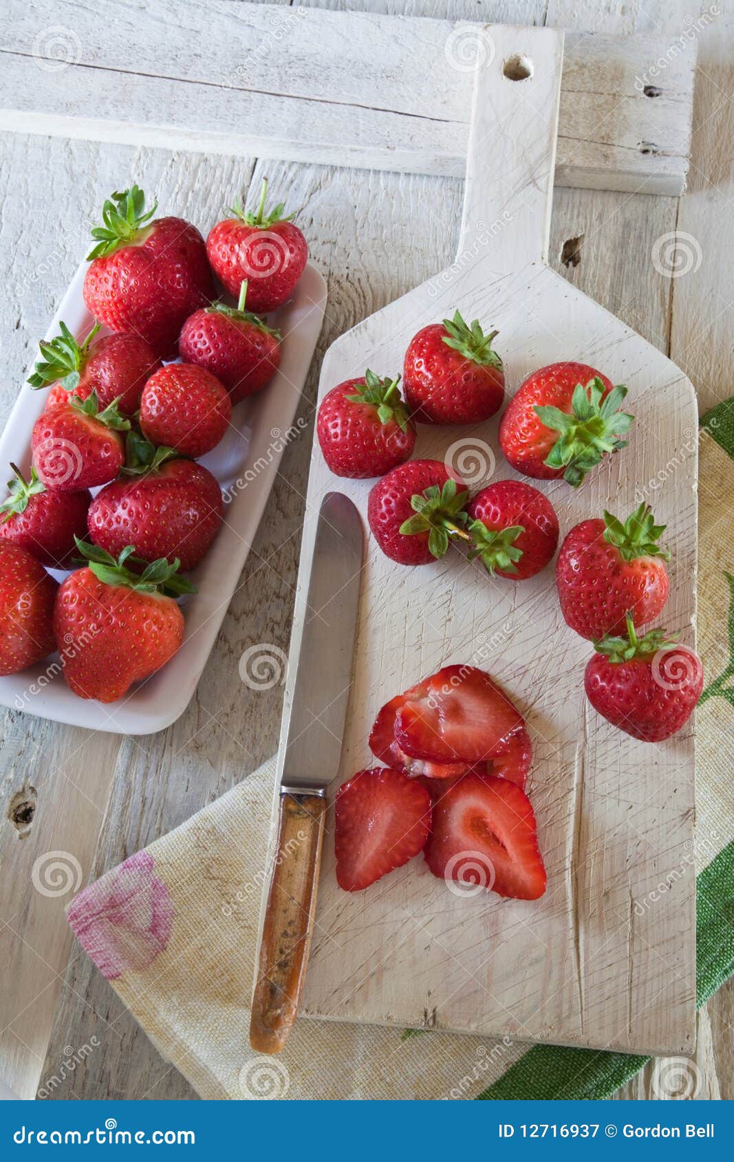 Fresas rebanadas en una tajadera. Fresas rebanadas y enteras en una tajadera blanca con un cuchillo viejo