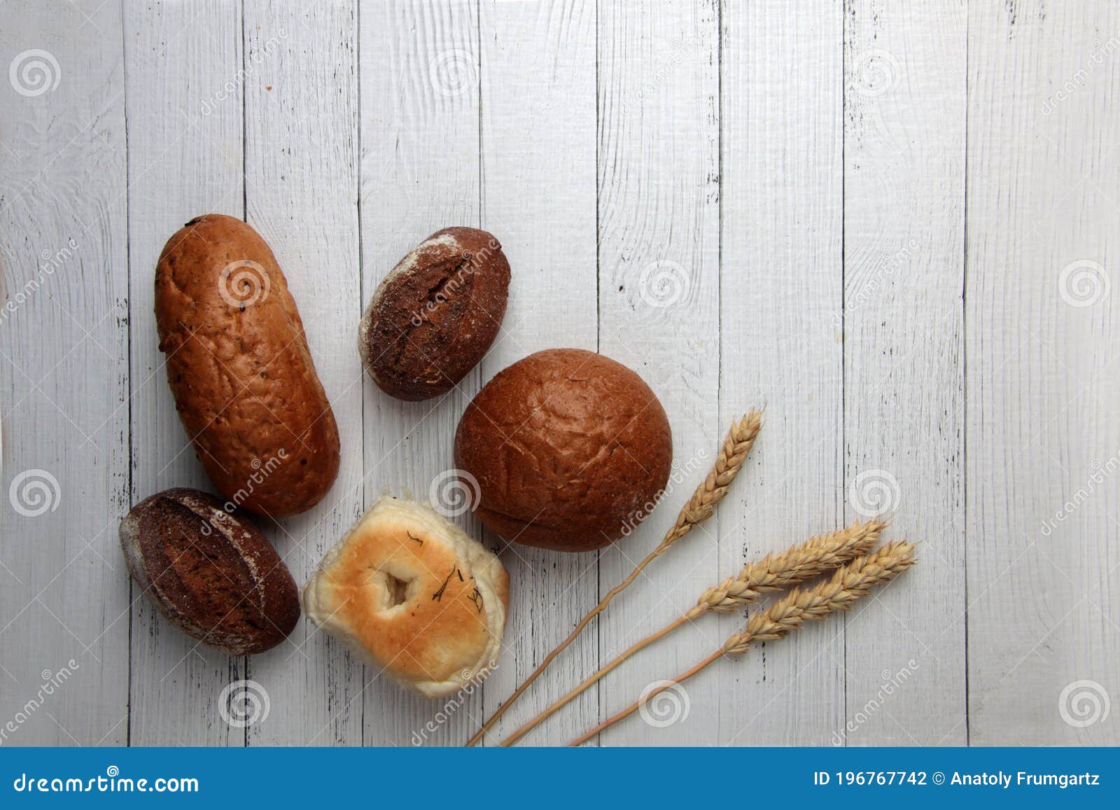 fresh bread - buns, baguette and ears of wheat on wooden background flat lay