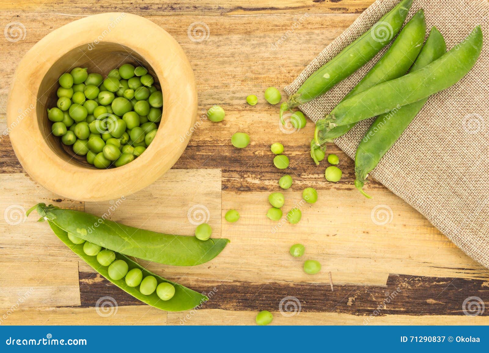 Fresh green peas in wooden bowl, on wooden surface and cloth