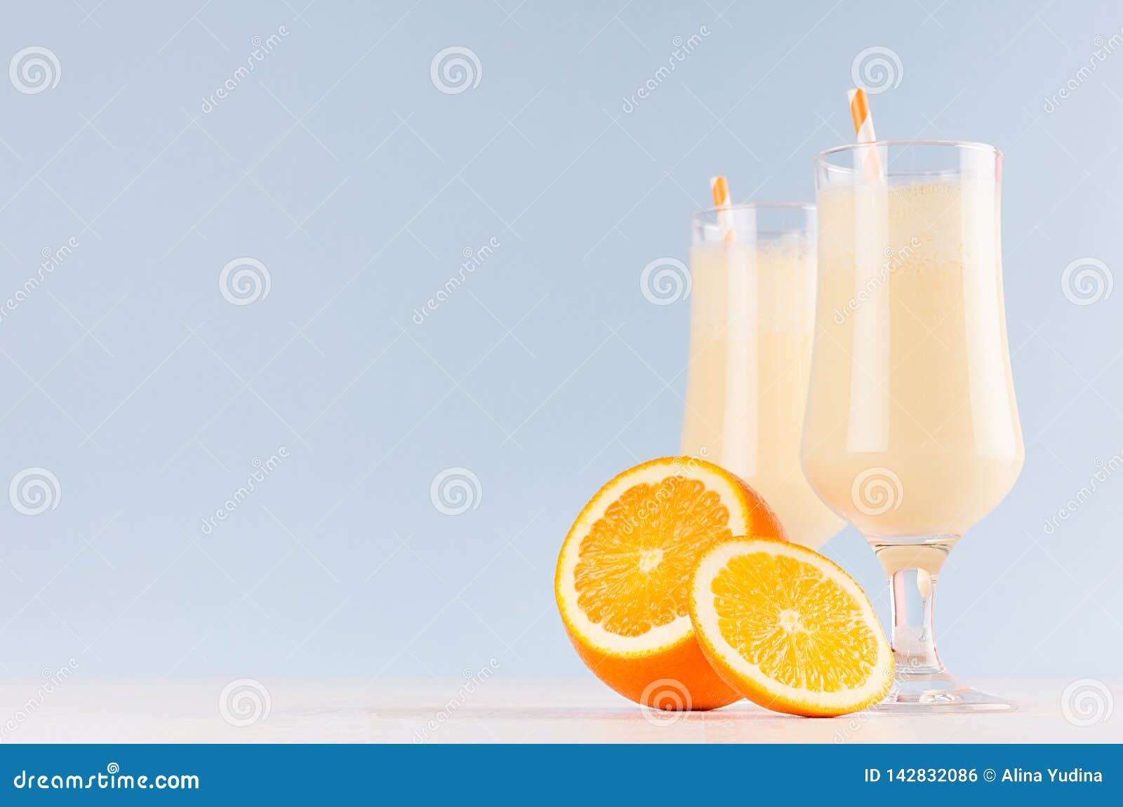 Fresh oranges milkshake with juicy pieces citrus and striped straw in gentle graceful soft light blue interior, copy space.