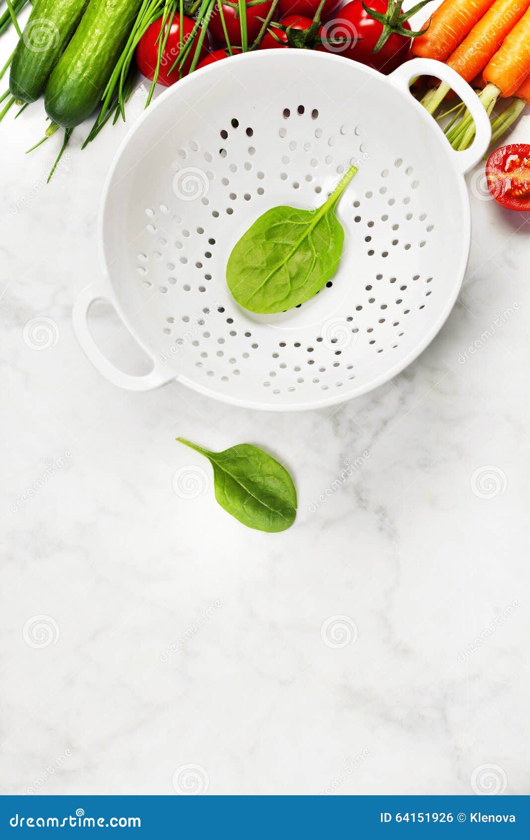 Fresh organic garden vegetables and colander bowl on white rustic stone background, healthy cooking concept