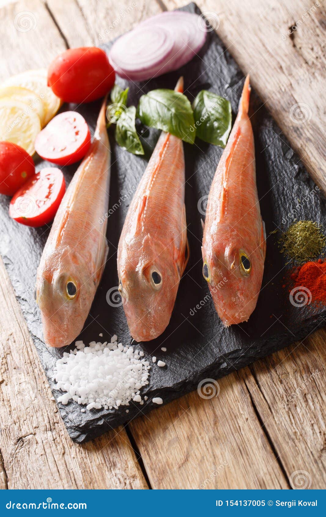 fresh raw triglidae, sea robins or gurnard fish with spices, vegetables and lemon closeup on a slate board. vertical