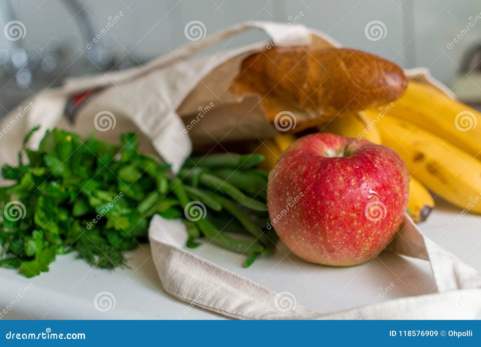 fresh ripe apple, bunch of parsley and green onion, bananas and french baguette in canvas reusable grocery tote bag on the kitchen