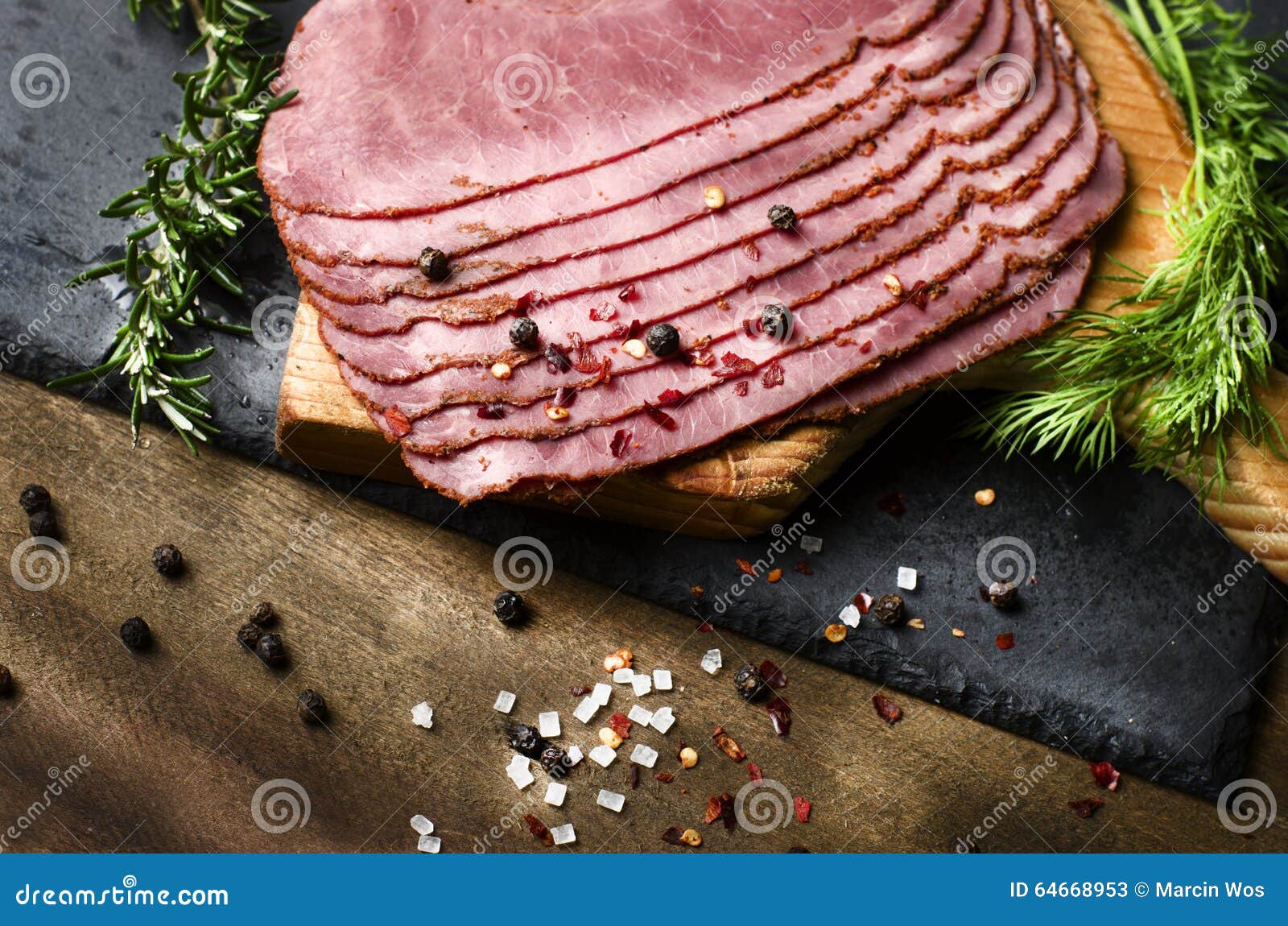 fresh sliced beef pastrami surrounded by herbs in wooden chopping board
