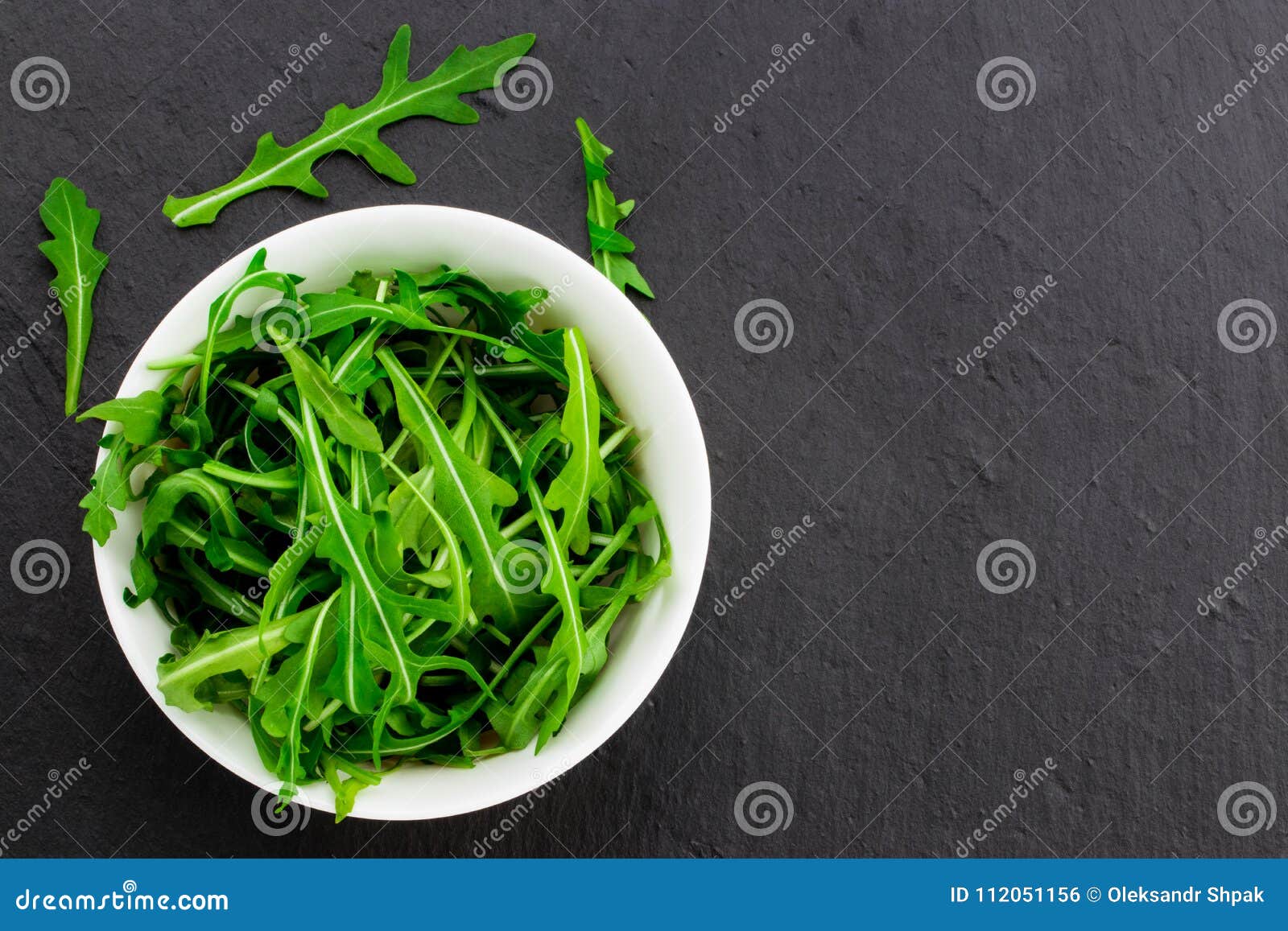fresh spring salad with rucola, in bowl on dark stone background