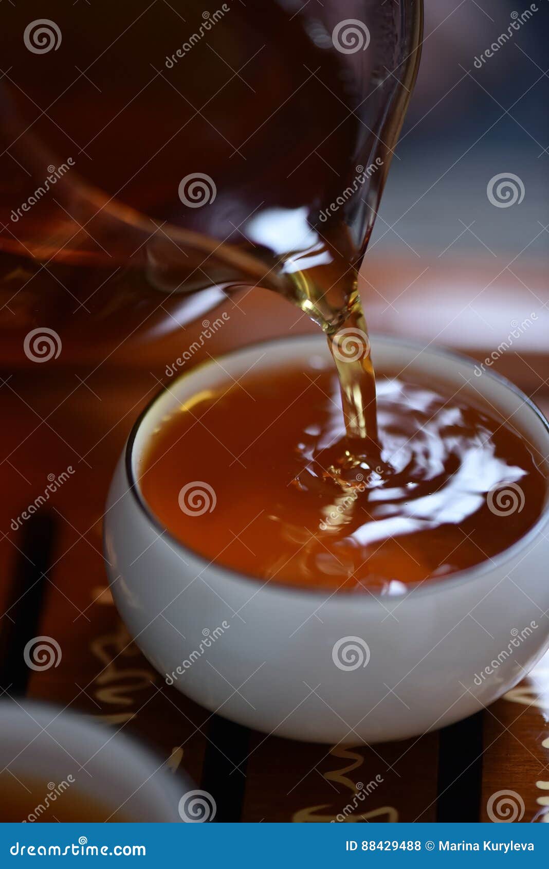 Fresh Tea Pouring from Glass Jug To White Ceramic Cup Stock Photo