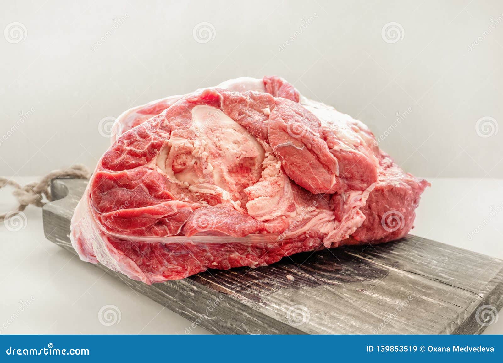 the freshest beef knuckle with bone lies on a wooden thick board on a light background. close-up. copy space