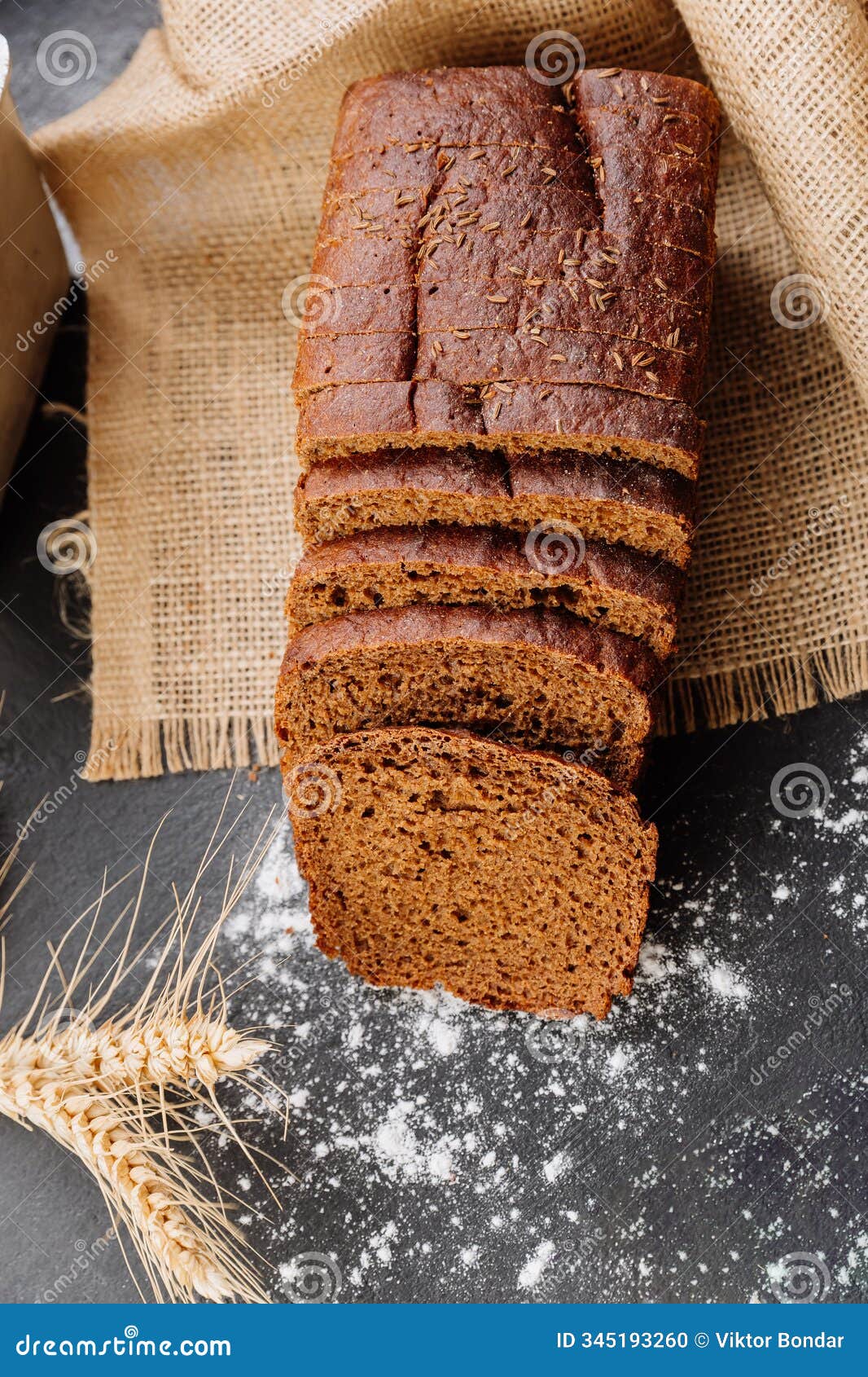 freshly sliced rye bread on burlap with wheat stalks and flour dust for rustic bakery presentation