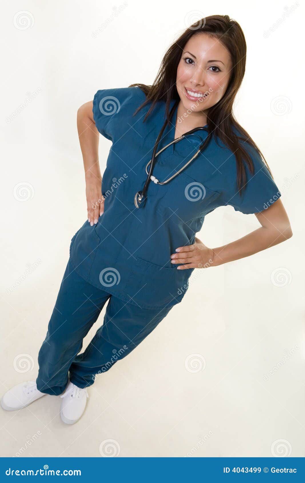 Freundliche Krankenschwester. Volle Karosserie einer Frauen-Gesundheitspflegearbeitskraft des attraktiven jungen Brunette hispanischen, die mit den Händen auf Hüften mit einem lächelnden freundlichen Ausdruck steht