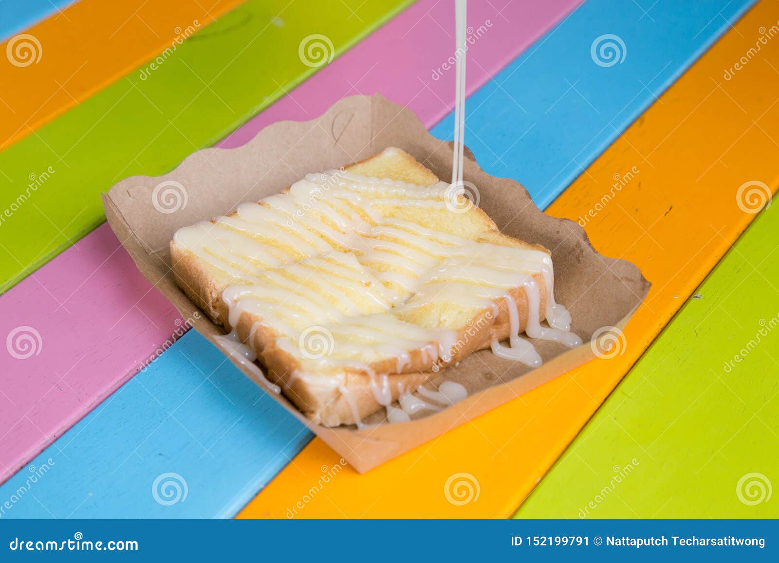 Toast Topped with Sweetened Condensed Milk in a Paper Dish on a Wooden Table. Stock Image