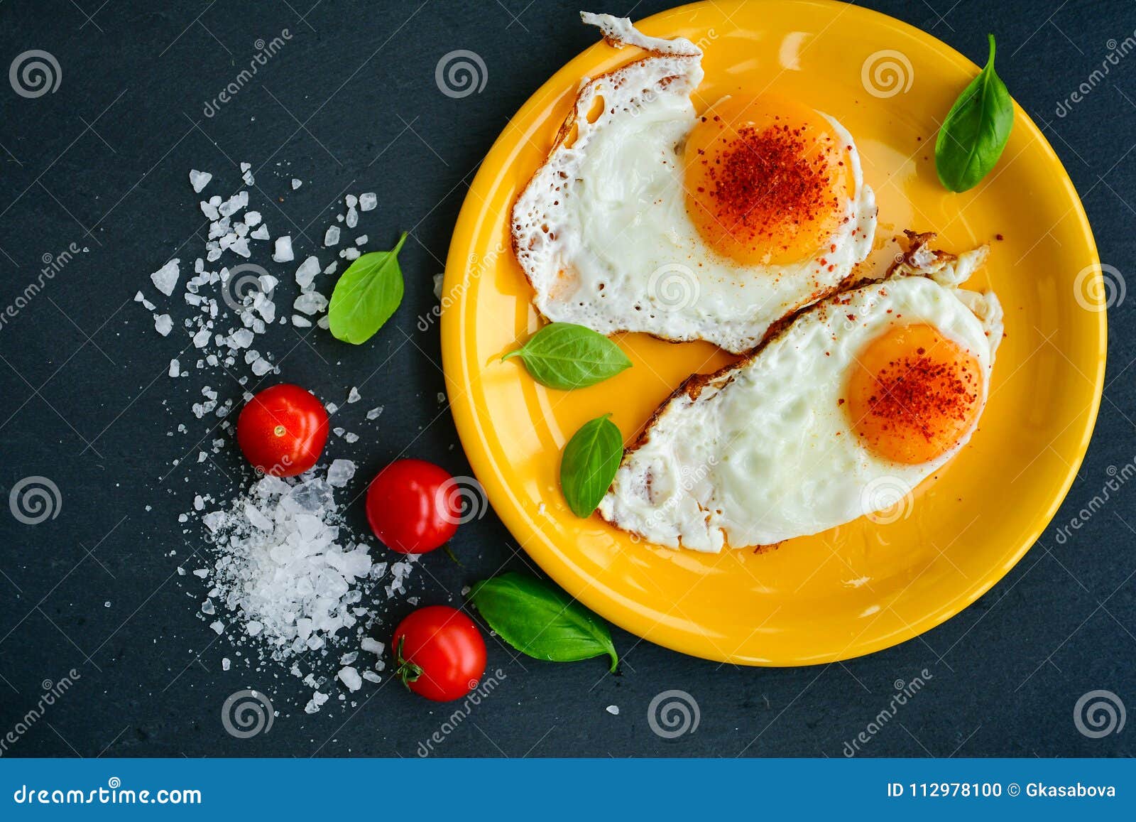 Fried Eggs. Bio Verse gebraden eieren, zout, vers basilicum, kersentomaten en brood op zwarte achtergrond