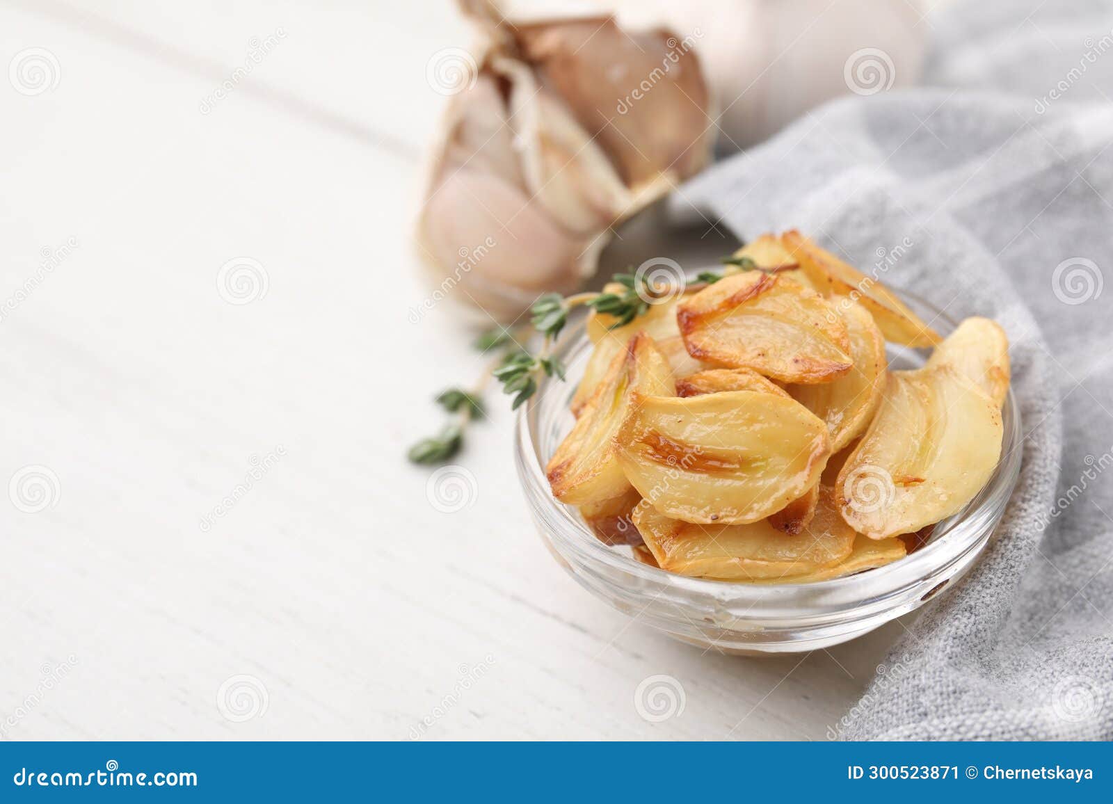 Fried Garlic Cloves and Thyme in Bowl on White Table, Closeup. Space