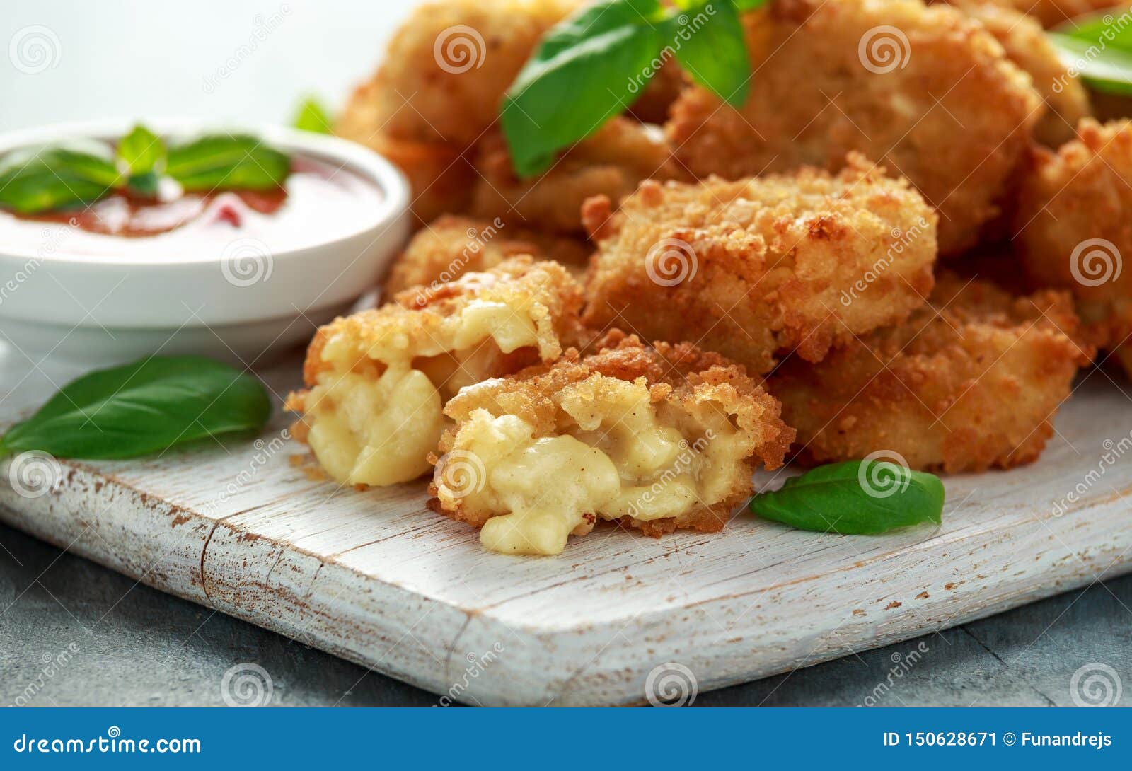 fried mac, macaroni and cheese bites in breadcrumbs with ketchup sauce on white wooden board