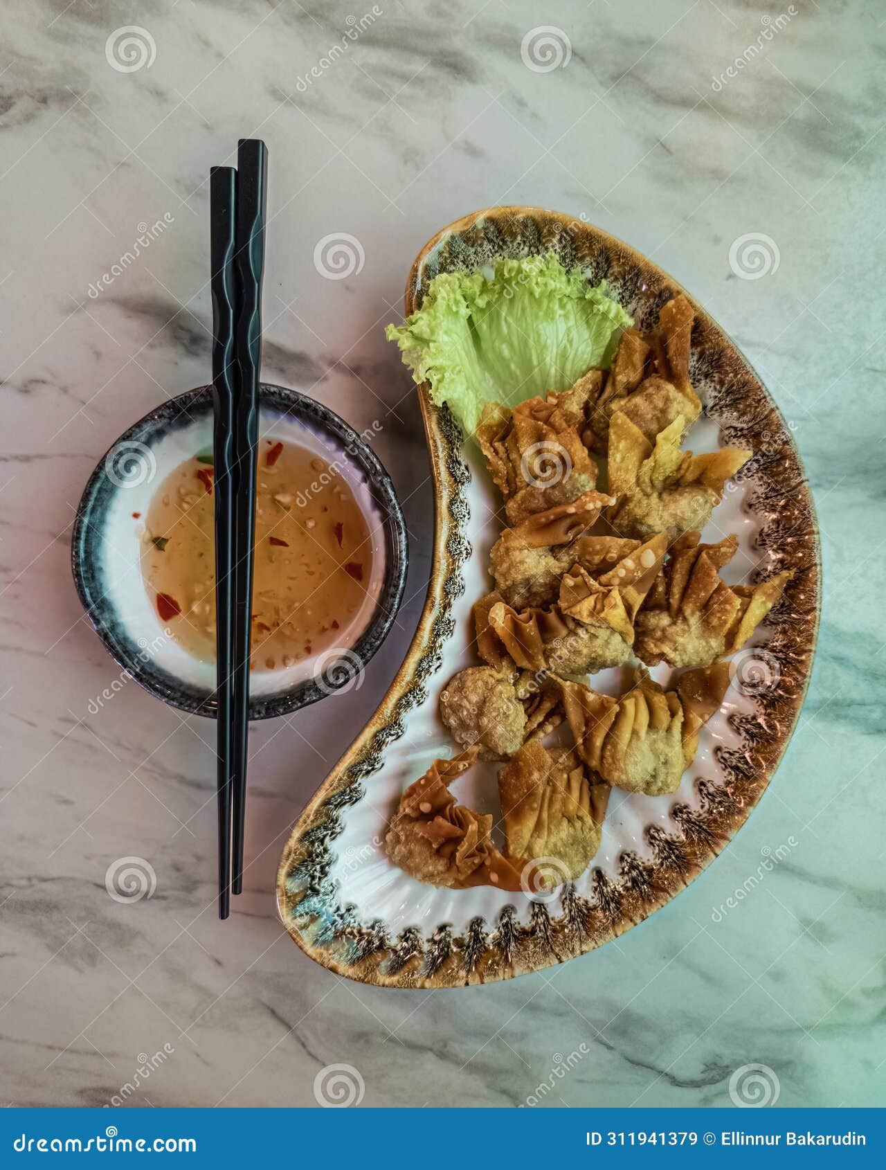 fried wantan served on the plate together with the dipping sauce and a pair of chopsticks. top view