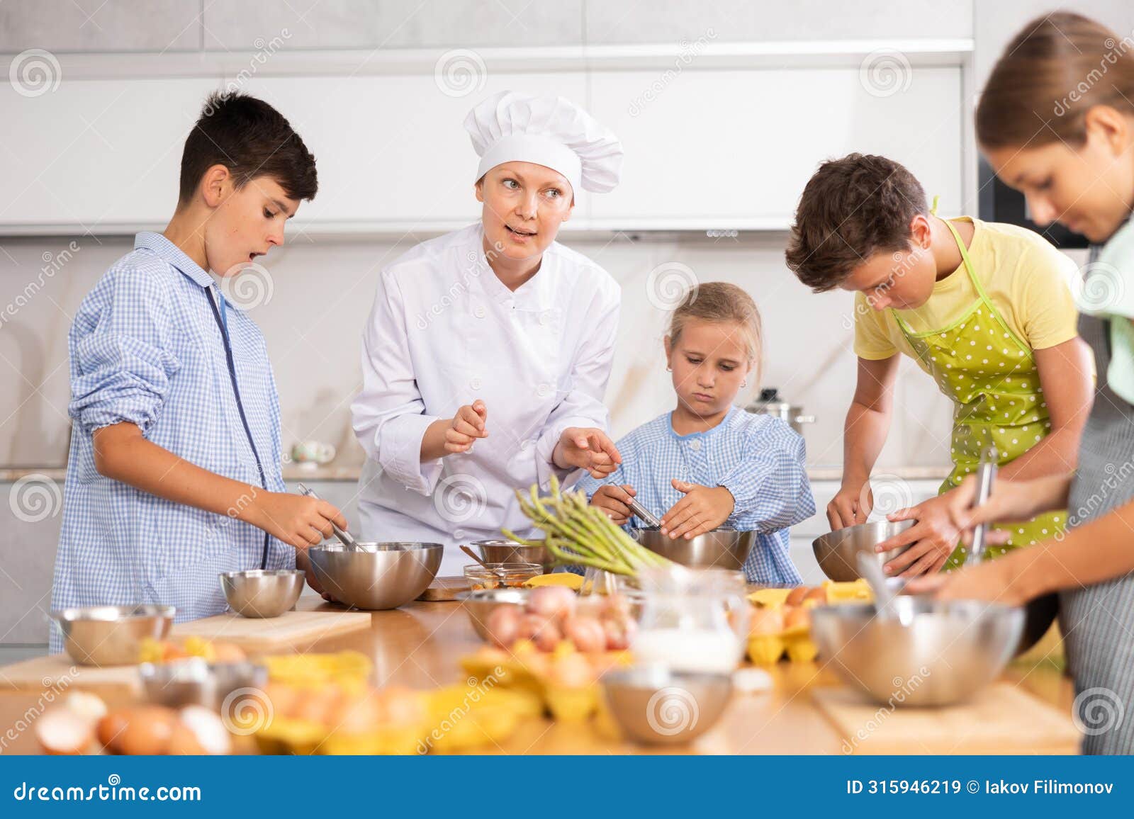 friendly female chef in white uniform giving culinary lesson to tweens
