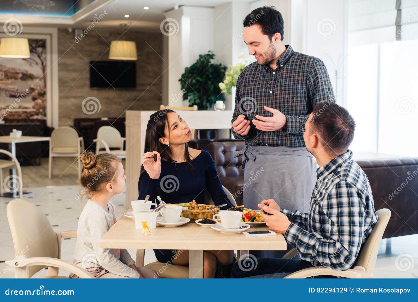 Friendly Smiling Waiter Taking Order At Table Of Family Having Dinner