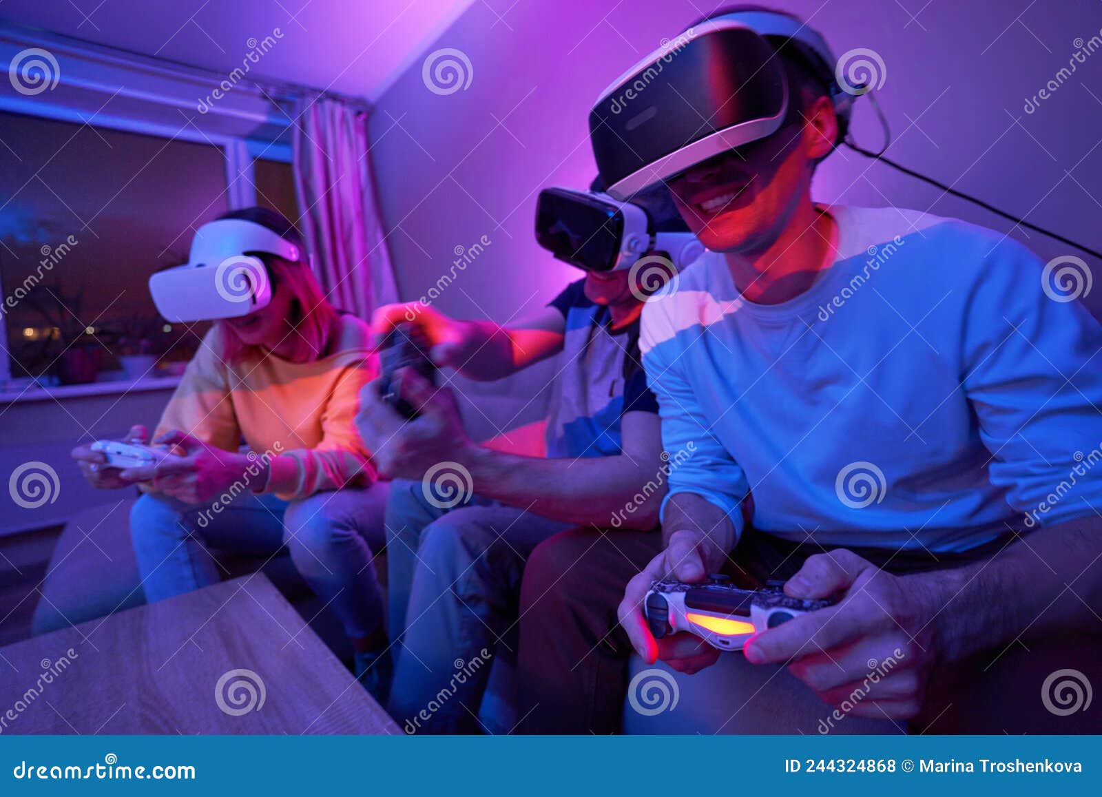 Friends Playing Virtual Reality Games Using Joysticks while Sitting on the Couch. Stock Photo