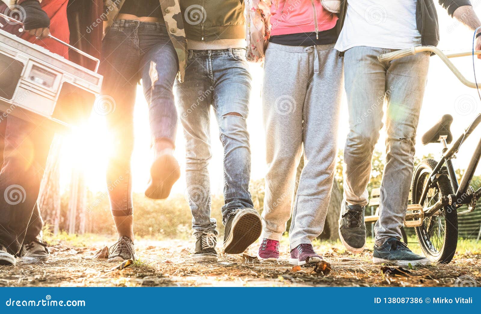 friends walking in city park with backlight and sunflare halo - millenial friendship concept and multiracial young people on