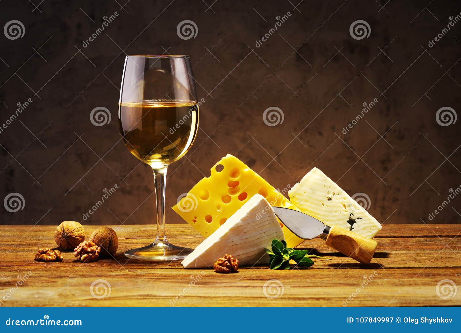 Fromage et vin dans un verre sur un conseil en bois. Fromage et un verre de vin blanc sur une vieille table en bois avec des écrous et un couteau pour le fromage