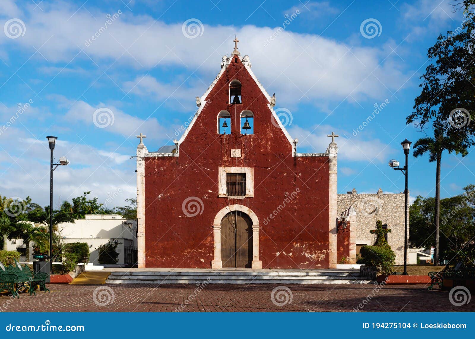 front of the red colonial church itzimna in a park with trees, merida, yucatan, mexico