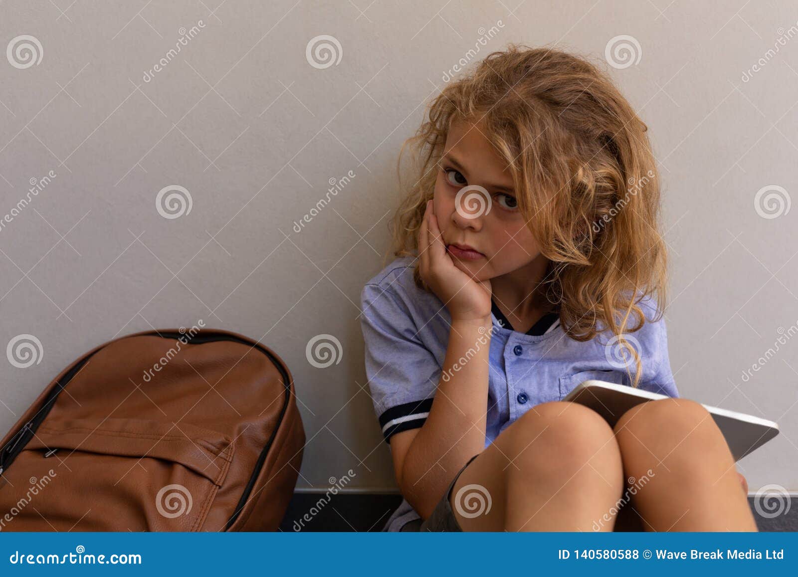 Schoolgirl With Her School Bag Sitting On Floor And Using Digital